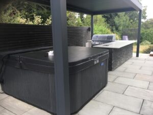 Outdoor kitchen with pergola, grey sandstone paving with black moodul feature wall.
